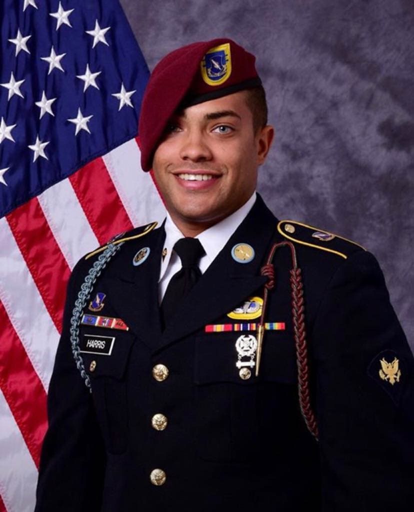 Smiling soldier in uniform with American flag.